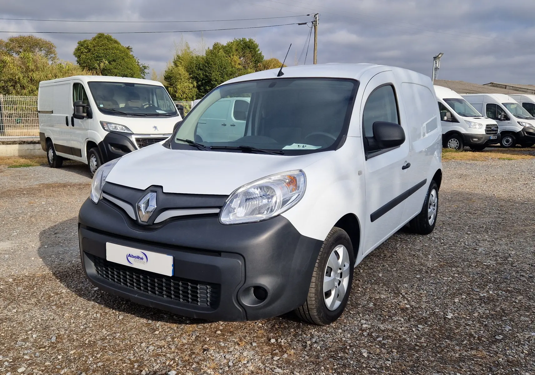Vue avant d'un Renault Kangoo blanc 2021 avec pare-chocs noir mat sur un parking extérieur.