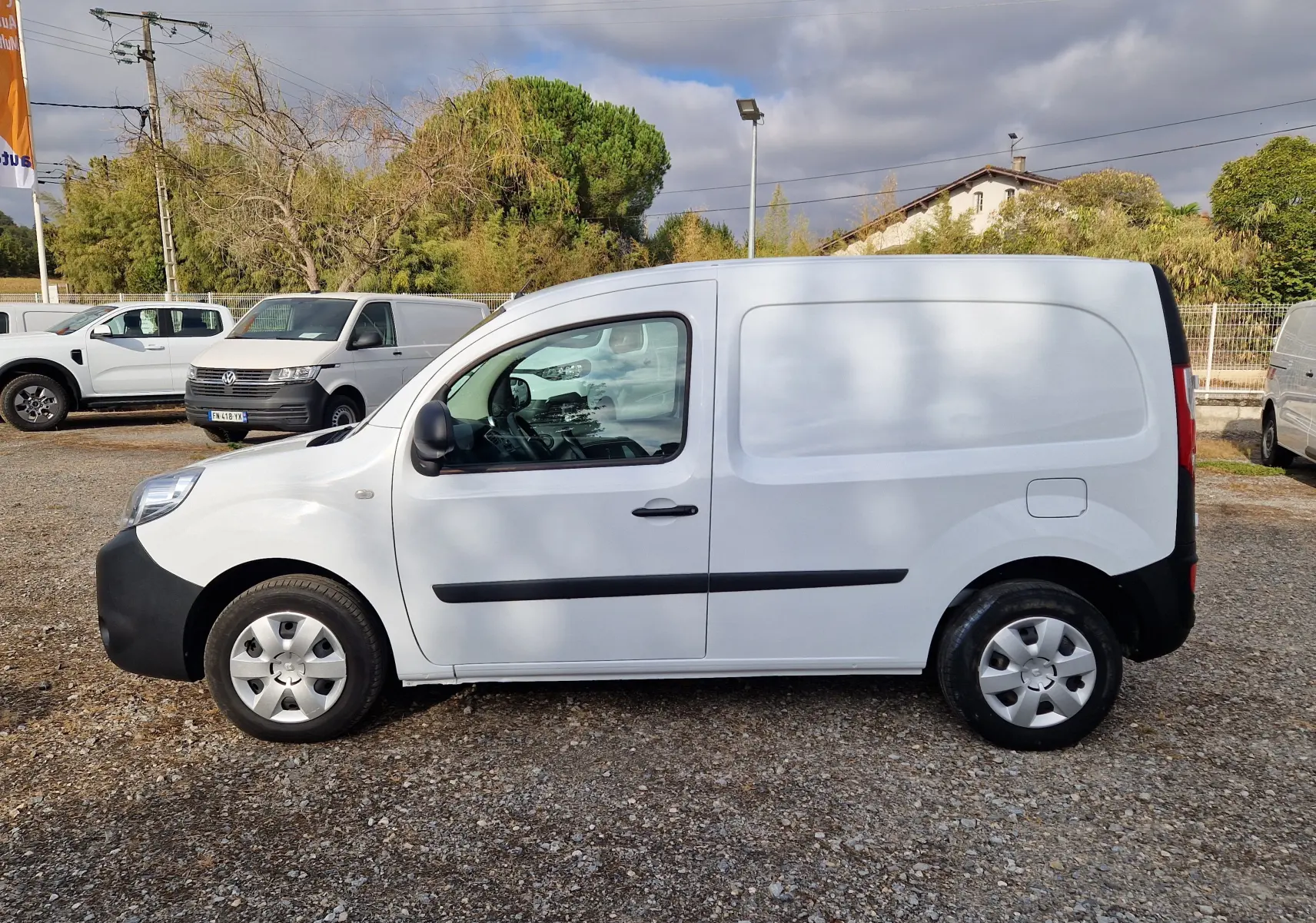 Renault Kangoo blanc vue de profil côté gauche, fourgonnette utilitaire avec protections noires sur les portières.