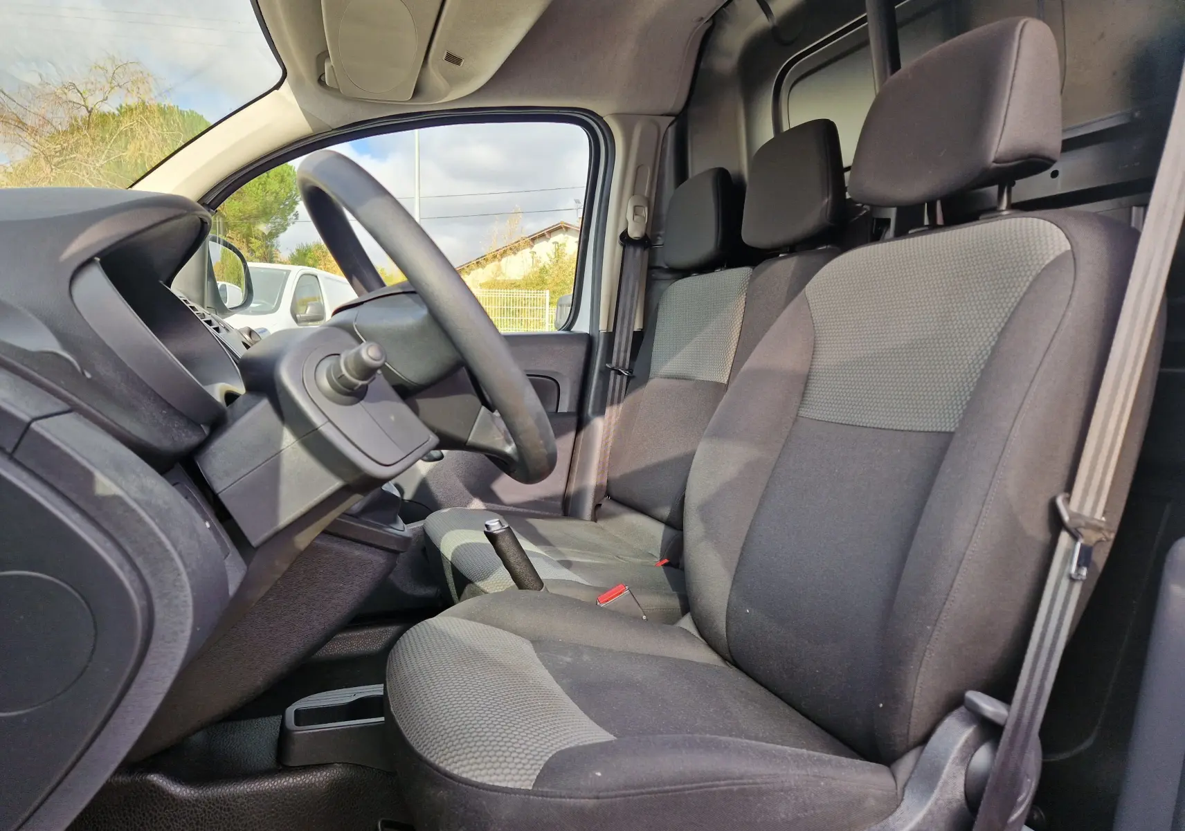 Vue intérieure côté conducteur du Renault Kangoo 2021, sièges tissu gris et volant noir, avec levier de vitesse manuel visible.