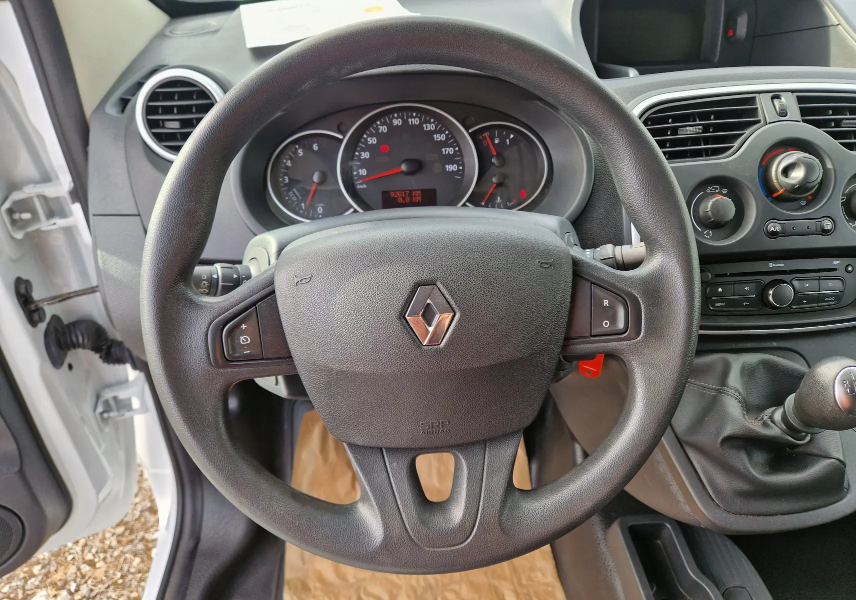 Vue intérieure centrée sur le volant noir du Renault Kangoo blanc 2021 avec tableau de bord et levier de vitesse manuel.