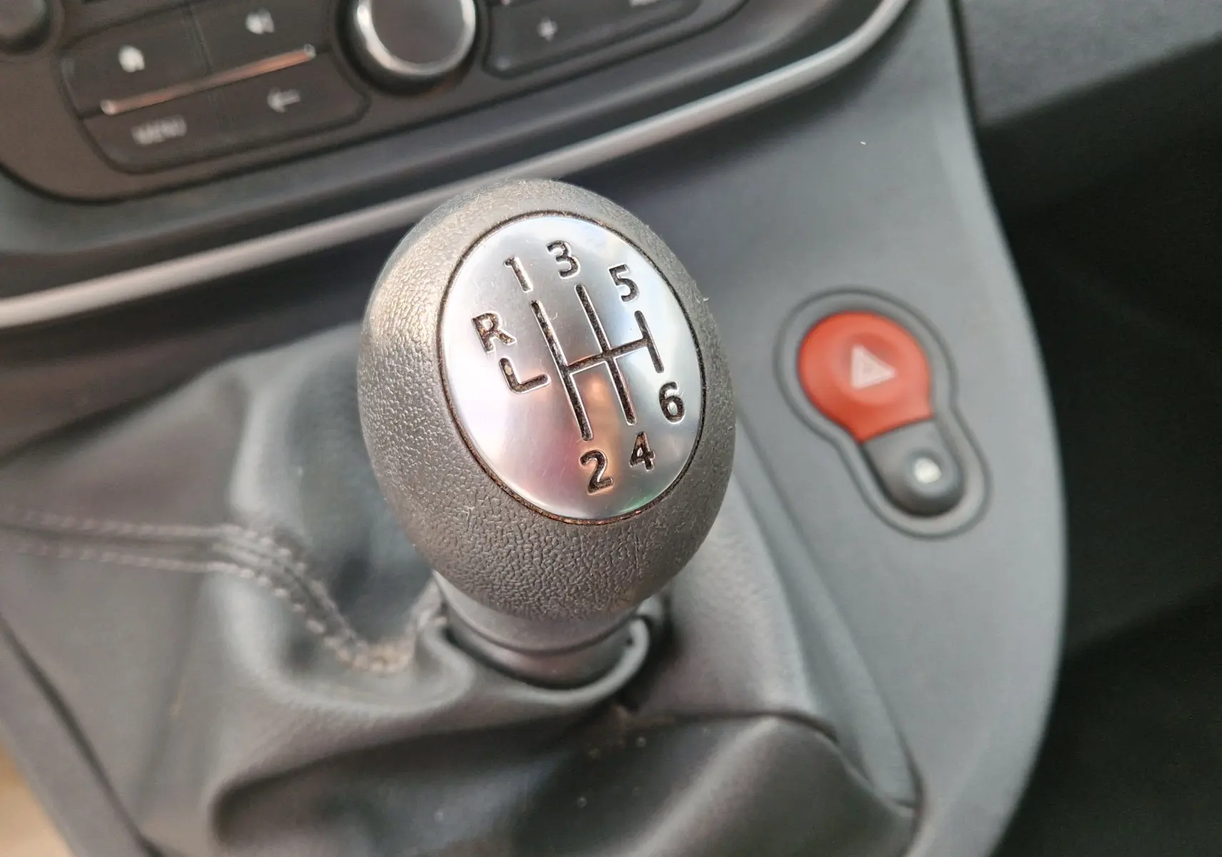 Gros plan sur le levier de vitesses manuel noir et chrome du Renault Kangoo blanc, avec bouton de warning rouge en arrière-plan.