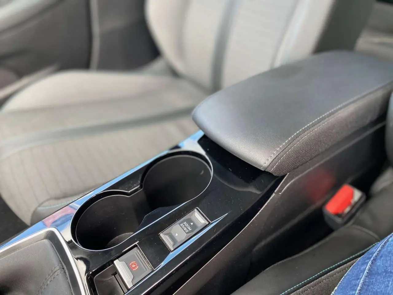 Gros plan sur la console centrale noire de la Peugeot 208 2021 avec accoudoir et commandes du frein à main électrique.