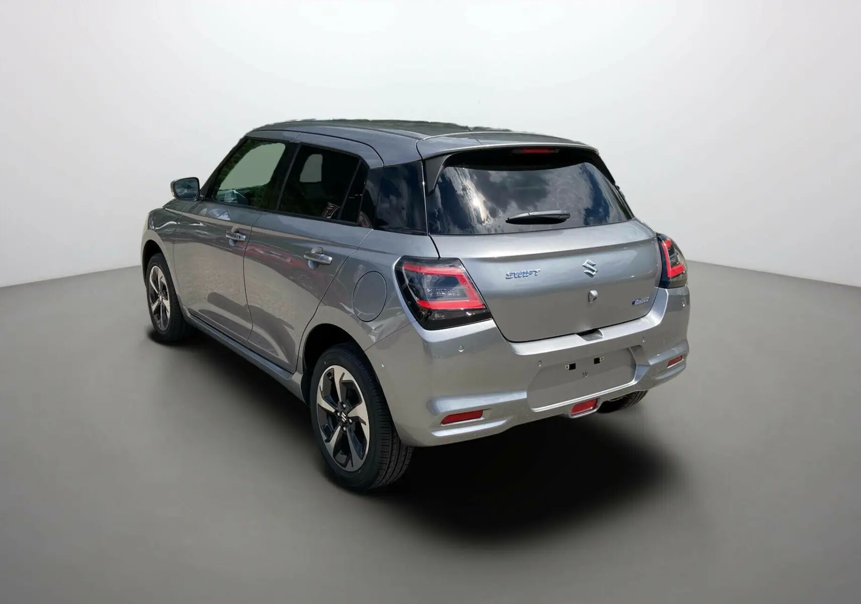 Vue 3/4 arrière droite d'une Suzuki Swift 2025 gris argent métallisé avec toit noir et vitres surteintées.