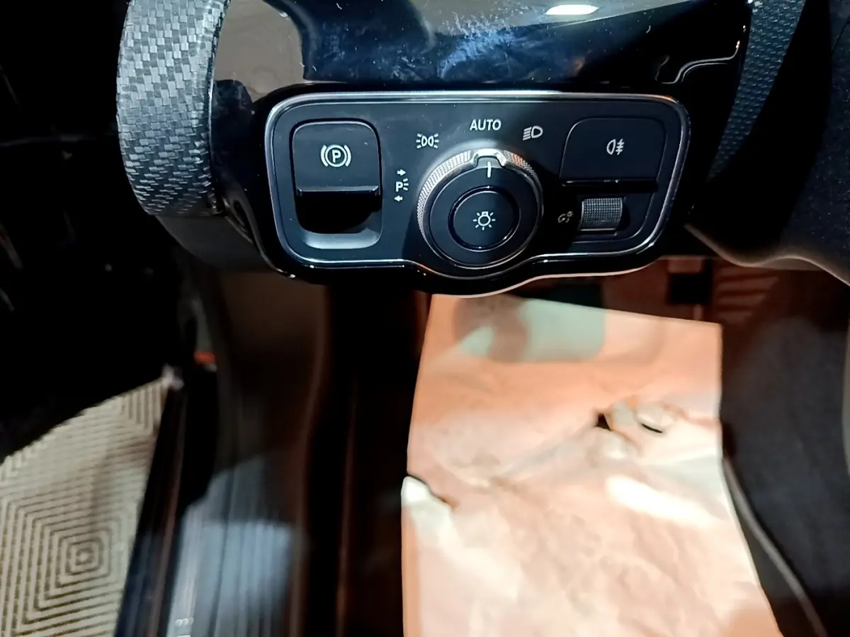 Gros plan sur le panneau de commande des phares et frein à main électrique dans l'habitacle noir d'une Mercedes Classe A 250 e.