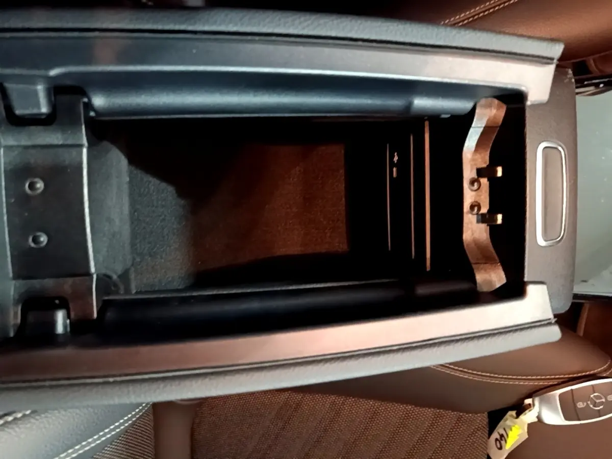 Vue plongeante sur l'accoudoir central ouvert et la clé Mercedes posée sur le siège en cuir marron.