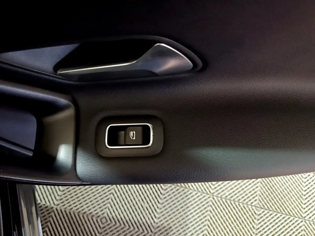 Gros plan sur la poignée intérieure et le bouton de verrouillage de la porte côté gauche d’une Mercedes Classe A noire.