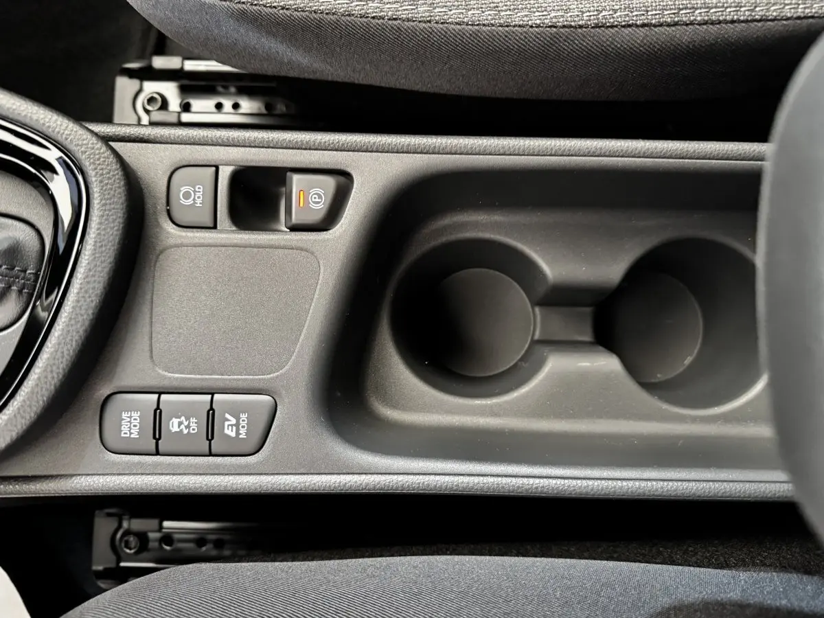 Vue en plongée sur la console centrale noire de la Toyota Yaris Cross 2026, avec boutons de mode de conduite et frein électrique.