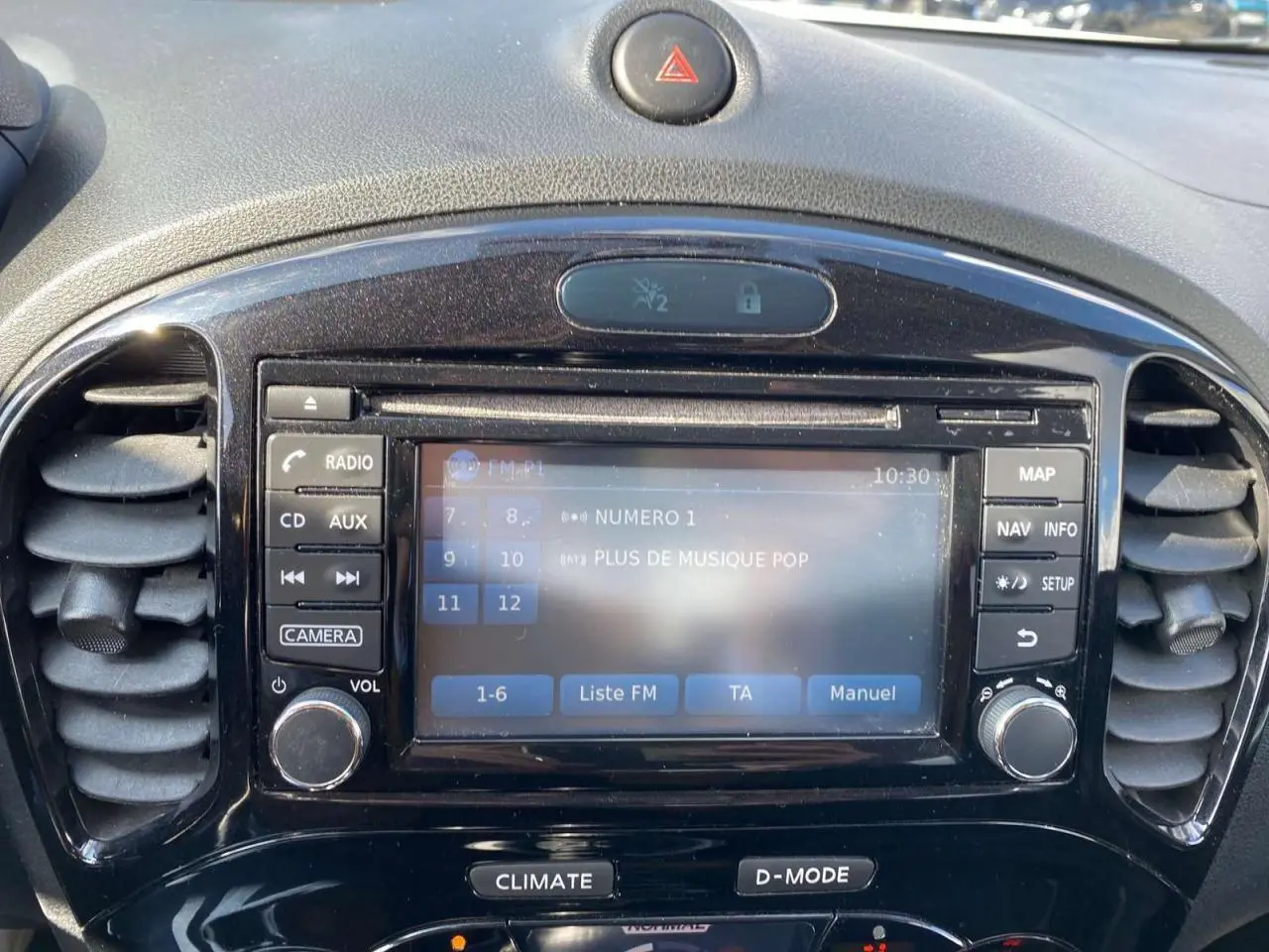 Vue rapprochée du tableau de bord noir du Nissan Juke avec écran tactile affichant la radio FM et commandes autour.
