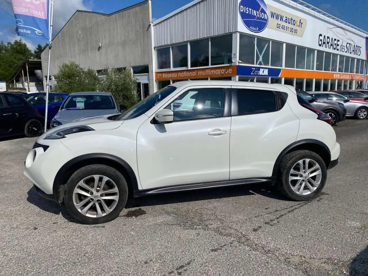 Profil côté gauche d'un Nissan Juke blanc 2017 avec jantes alliage 17 pouces, stationné devant un garage.