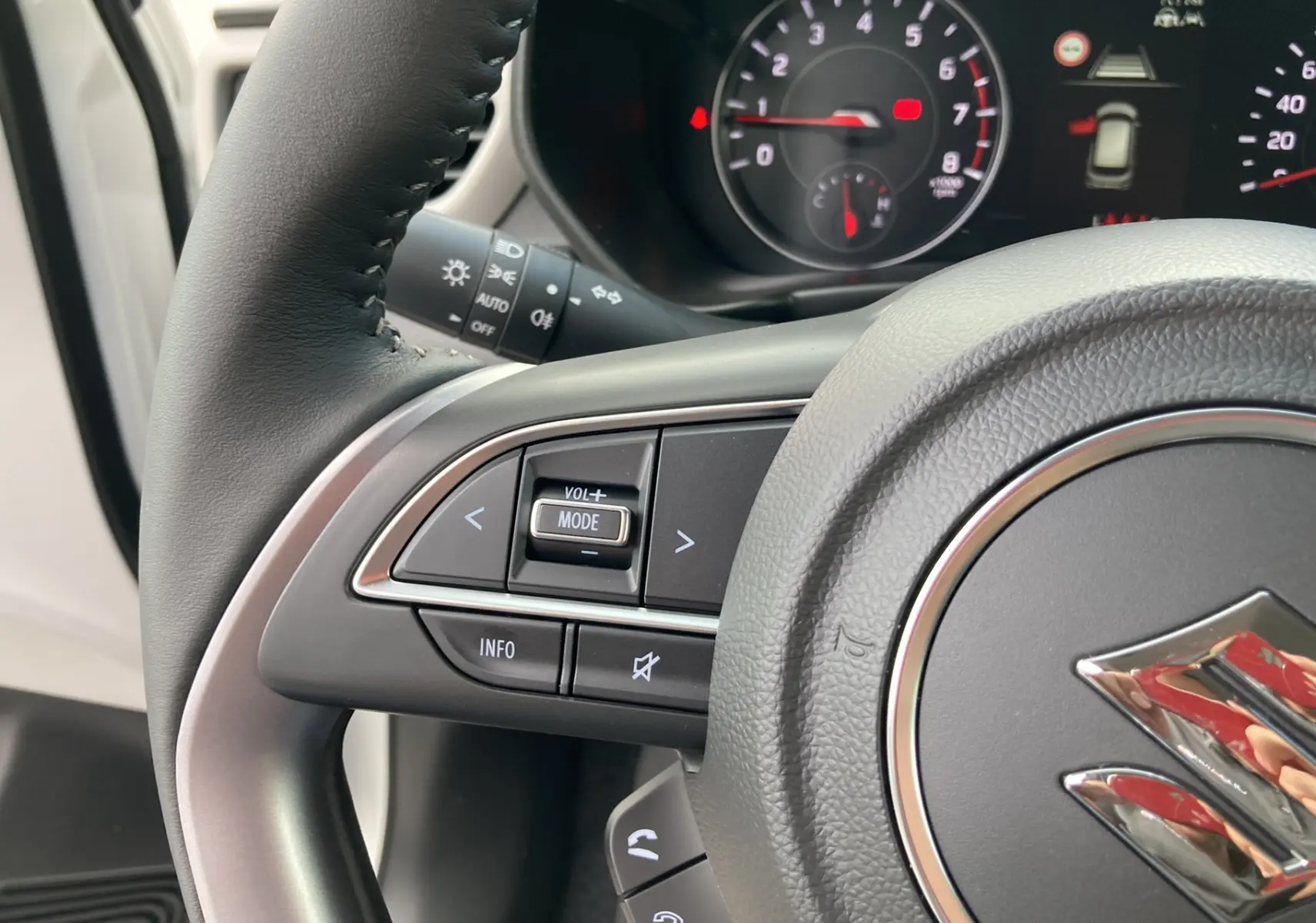 Gros plan sur le volant cuir multifonctions de la Suzuki Swift 2025, avec commandes audio et tableau de bord partiellement visible.