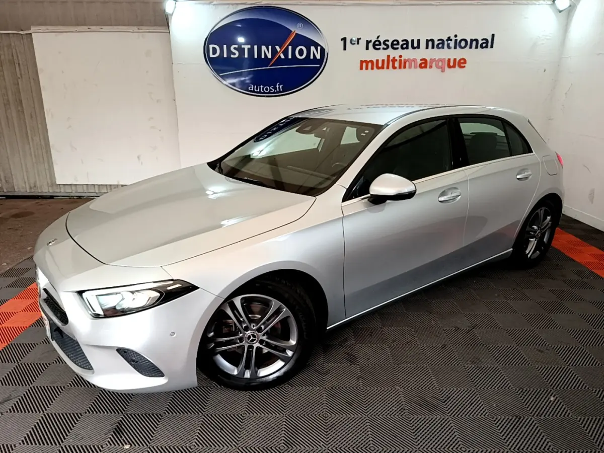 Vue 3/4 avant droite d'une Mercedes Classe A A 180 d Business Line gris clair, avec jantes alliage et phares LED allumés.