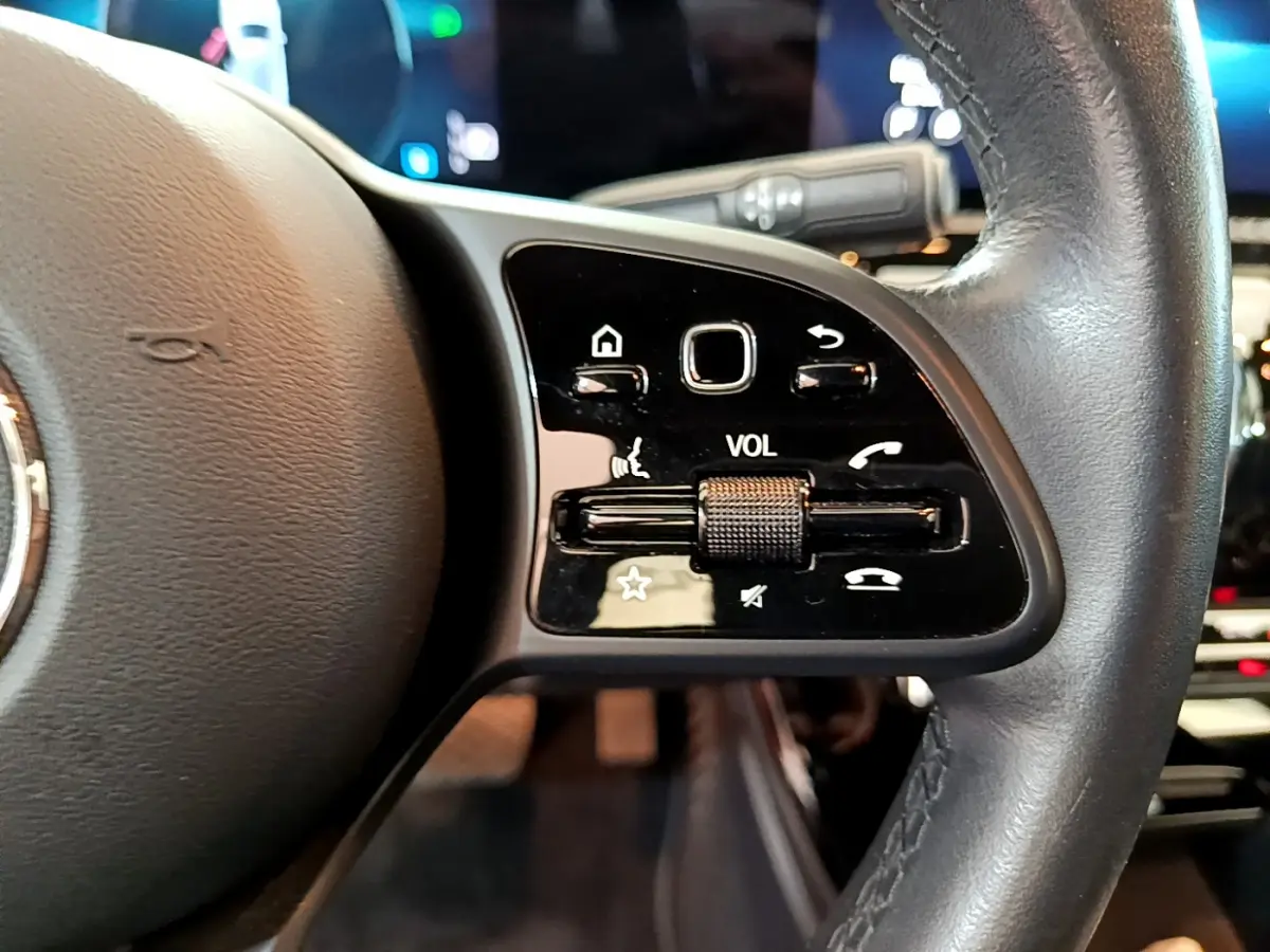 Gros plan sur les commandes de volume et fonctions vocales au volant cuir noir de la Mercedes Classe A 180 d Business Line 2020.