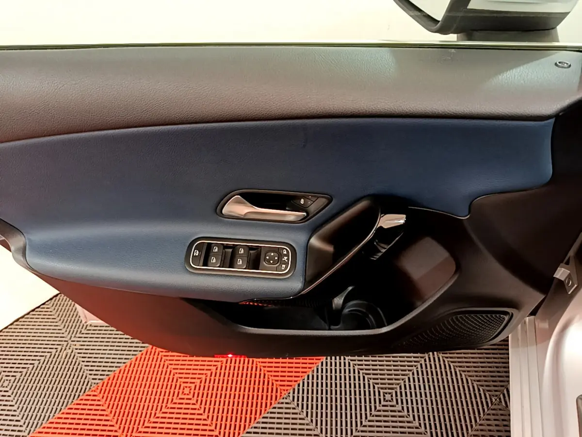 Vue intérieure du panneau de porte côté conducteur d'une Mercedes Classe A 180 d Business Line gris clair, avec commandes de vitres et poignée chrome.