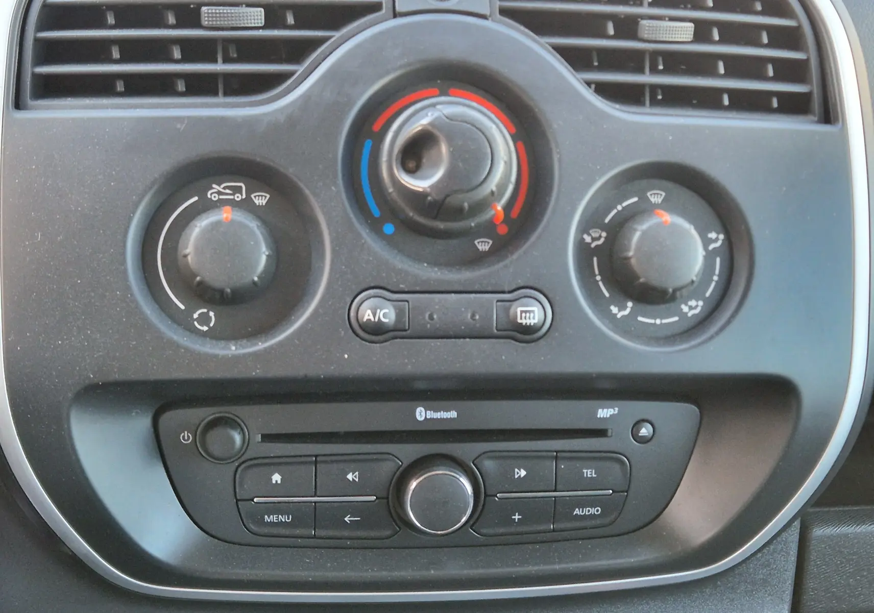 Détail du tableau de bord du Renault Kangoo blanc 2021, montrant les commandes de climatisation et la radio avec Bluetooth.