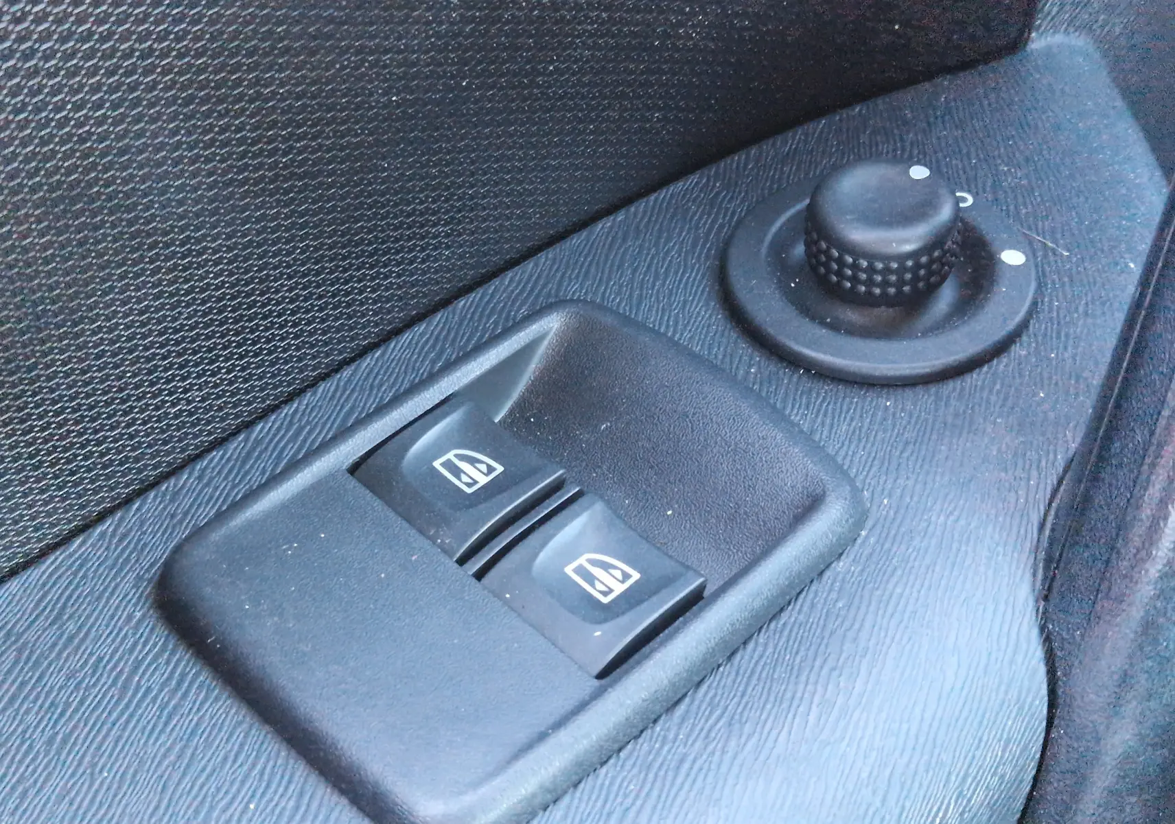 Gros plan sur les commandes de lève-vitres et réglage des rétroviseurs côté gauche d’un Renault Kangoo blanc 2021.