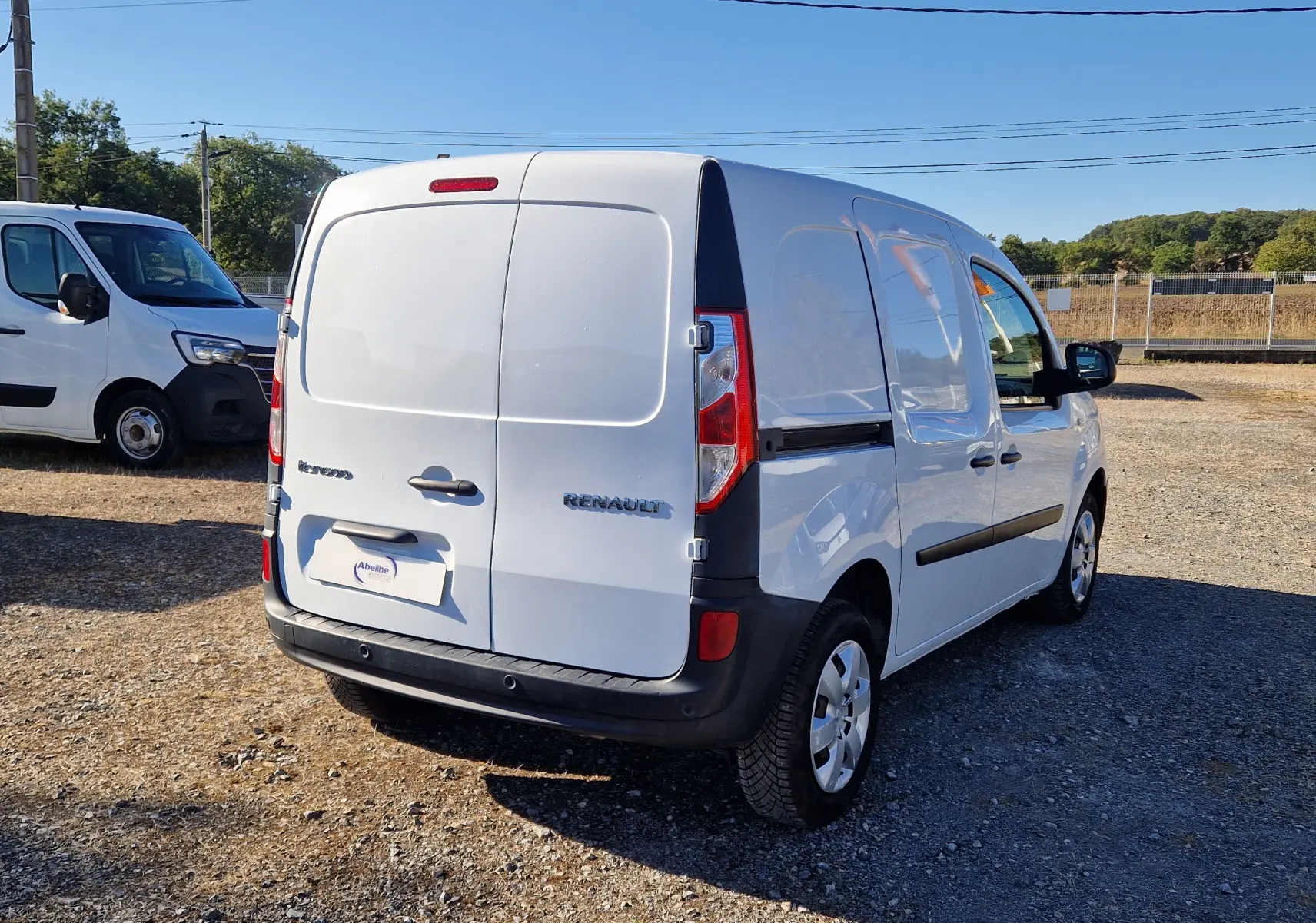 Renault Kangoo blanc vue 3/4 arrière droit, fourgonnette utilitaire avec portes arrière battantes, stationné en extérieur.