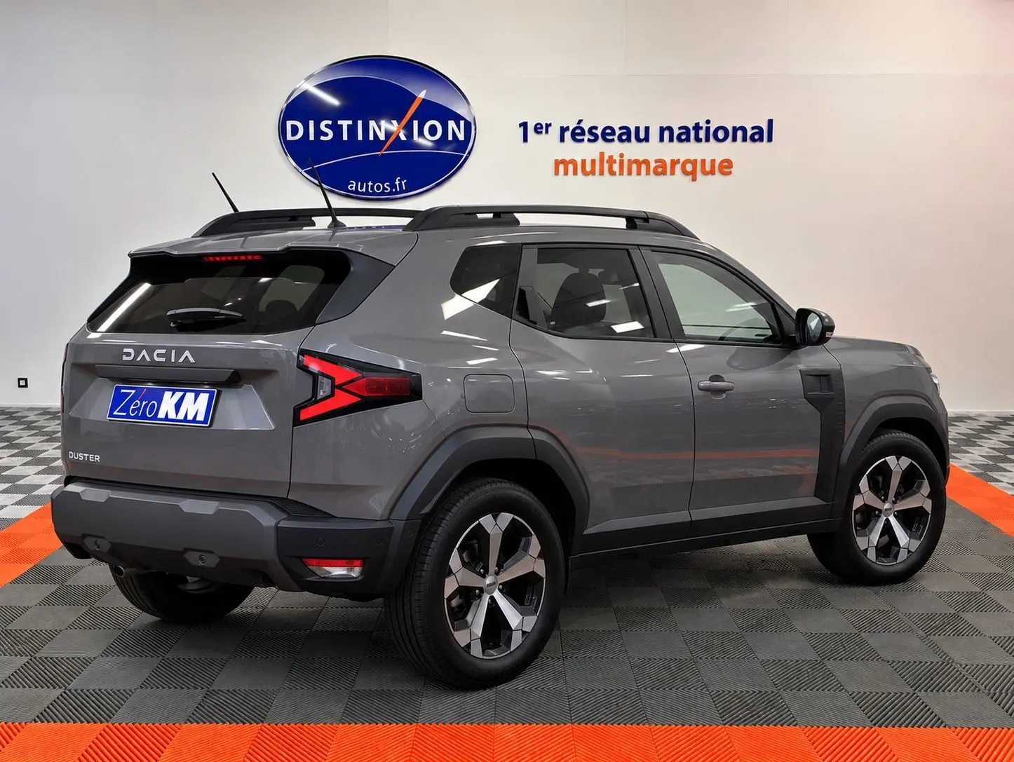 Vue 3/4 arrière droite du Dacia Duster gris schiste 2026 avec jantes alliage et barres de toit noires.