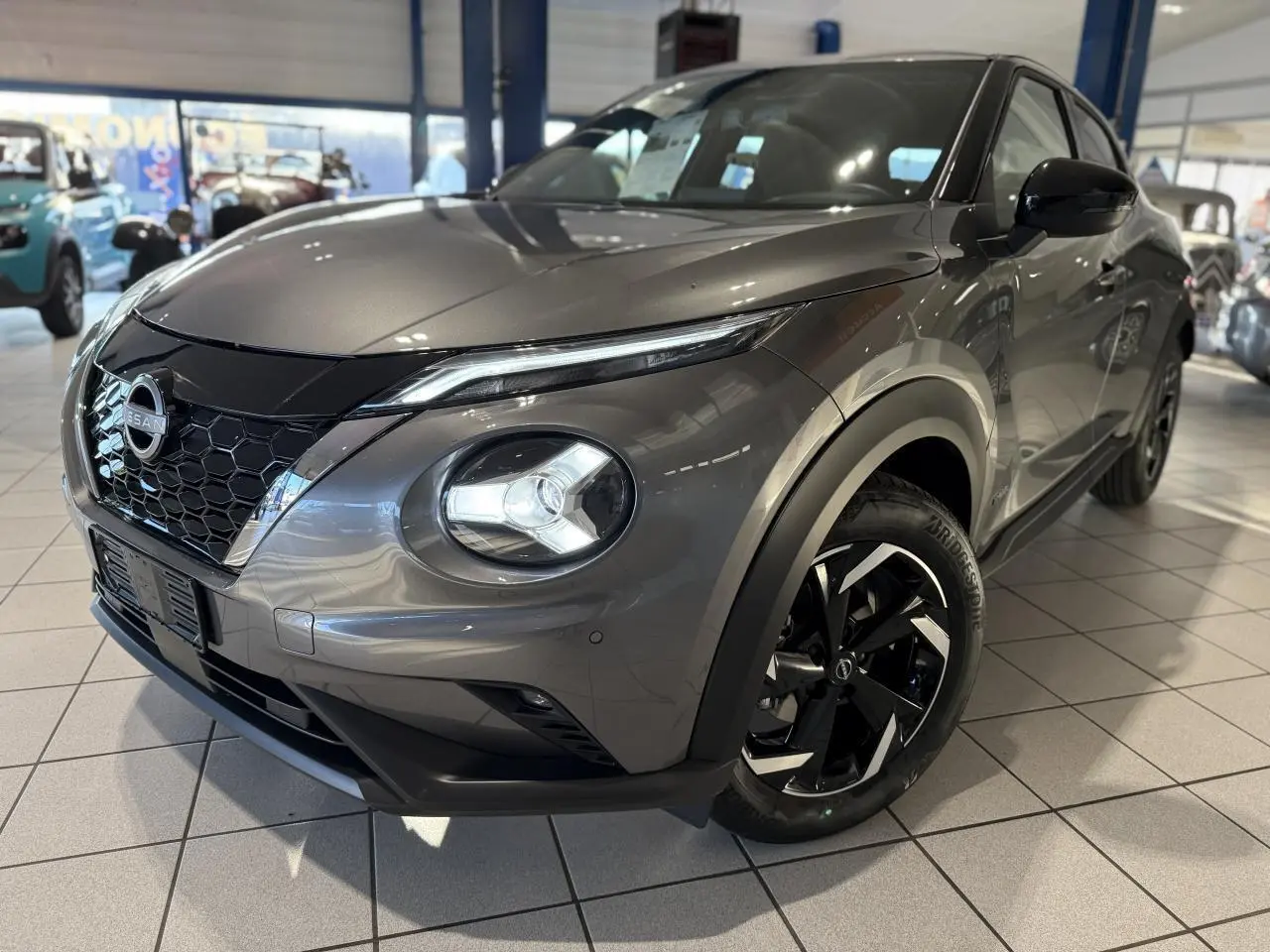 Nissan Juke Hybrid 143 N-Connecta gris métallisé en 3/4 avant droit avec jantes alliage noires et calandre en nid d'abeille.