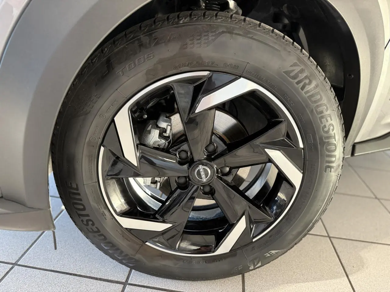 Gros plan sur la jante alliage 17 pouces noire et argentée du Nissan Juke Hybrid gris métallisé côté gauche.