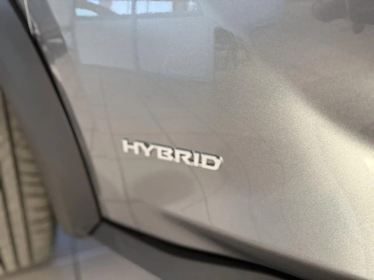 Gros plan sur l’inscription Hybrid sur la portière côté gauche d’un Nissan Juke gris métallisé 2024.