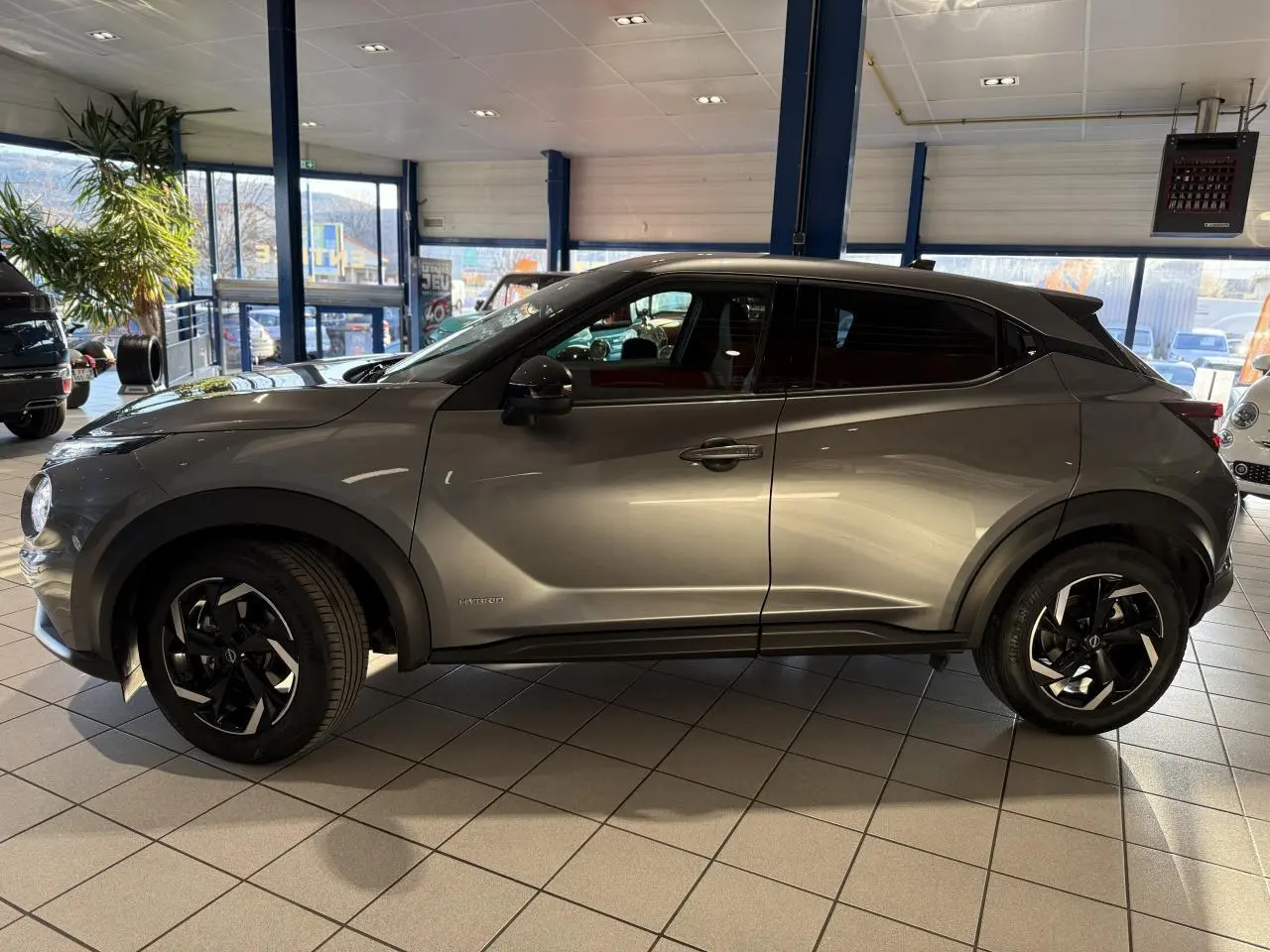 Profil côté gauche du Nissan Juke Hybrid 143 N-Connecta gris métallisé en showroom avec jantes alliage noires.