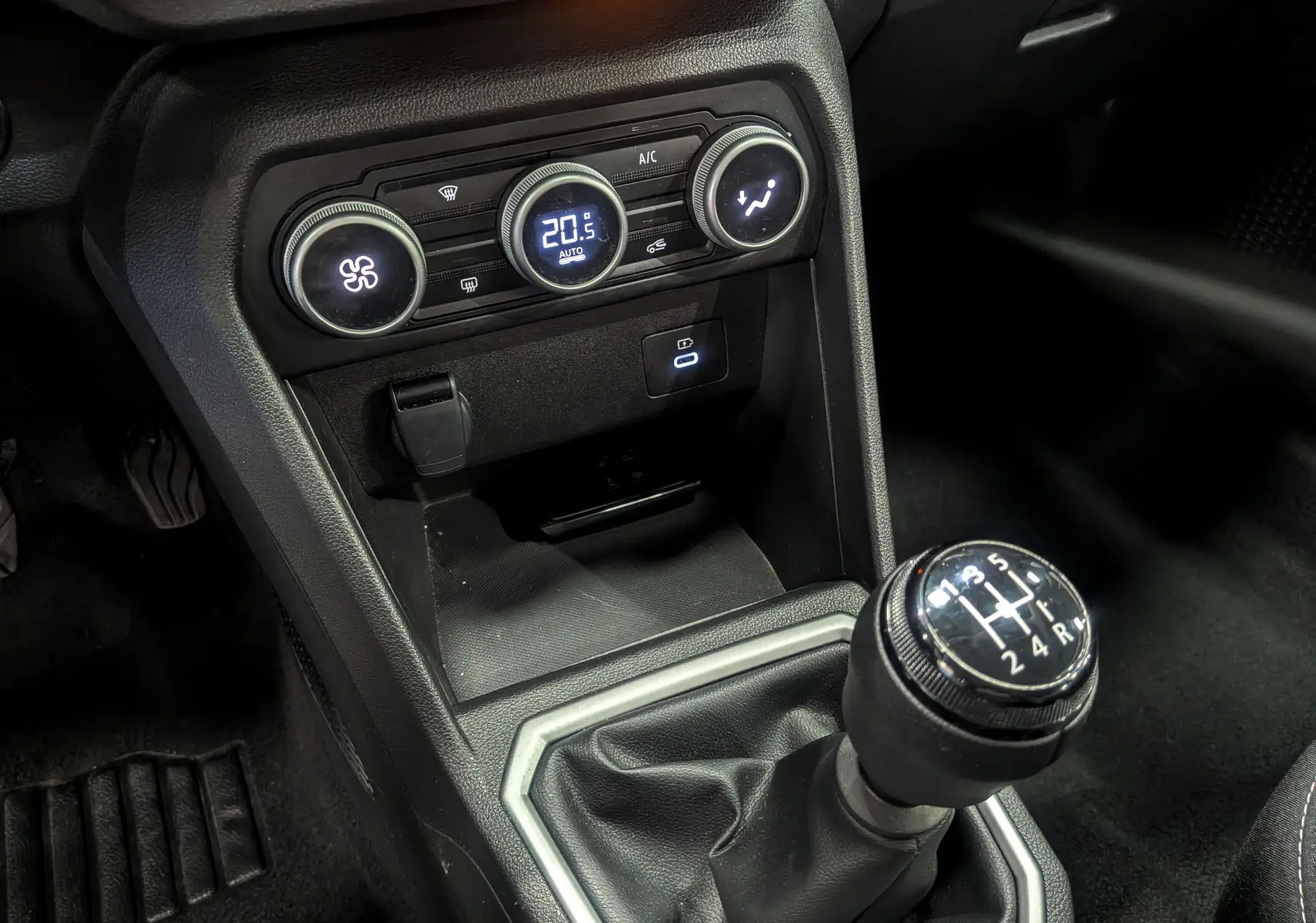 Gros plan sur la console centrale de la Dacia Sandero TCe 90 CH Journey 2025, avec levier de vitesses manuel et commandes de climatisation.