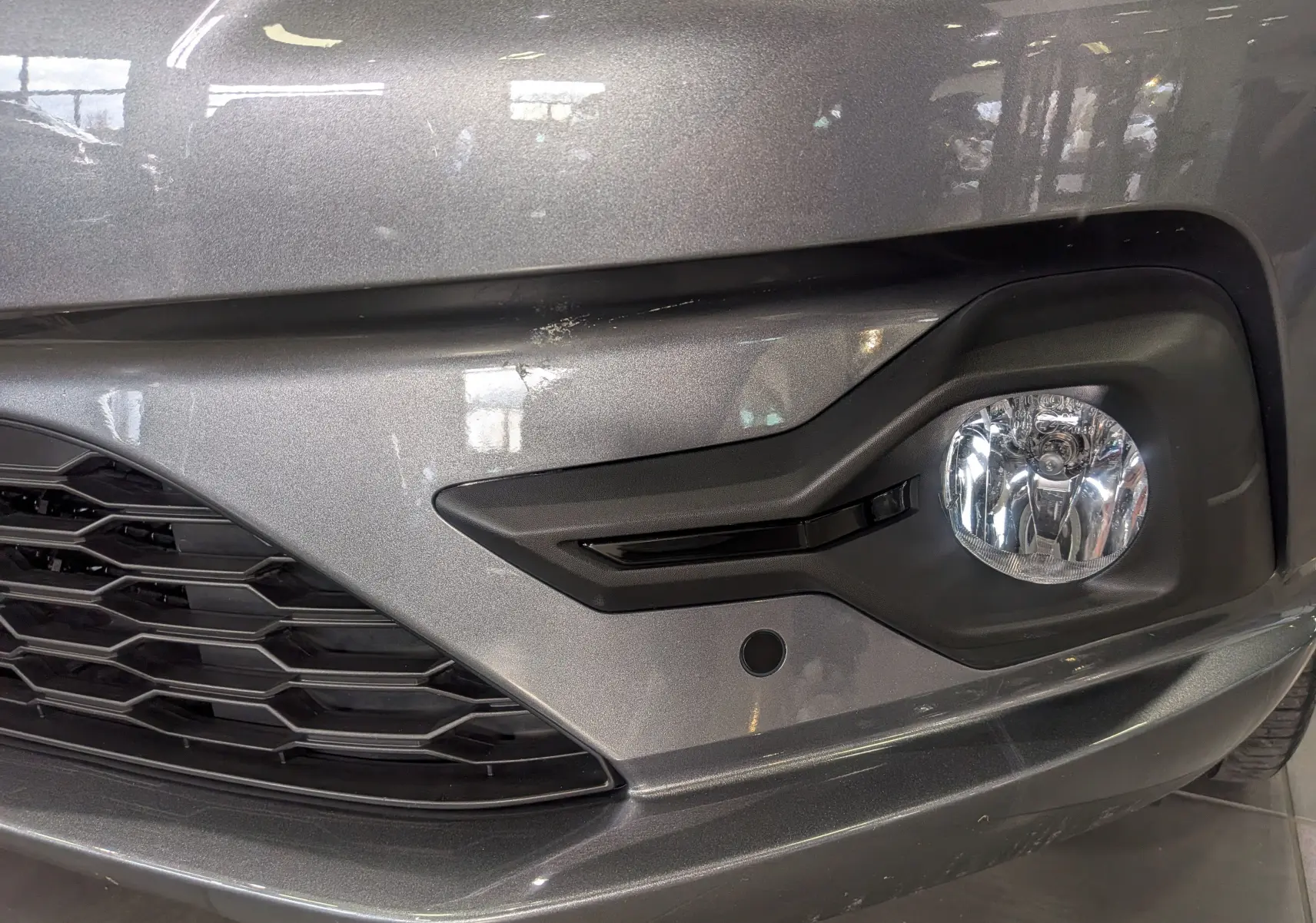 Gros plan sur le pare-chocs avant droit gris schiste de la Dacia Sandero TCe 90 CH Journey avec antibrouillard intégré.