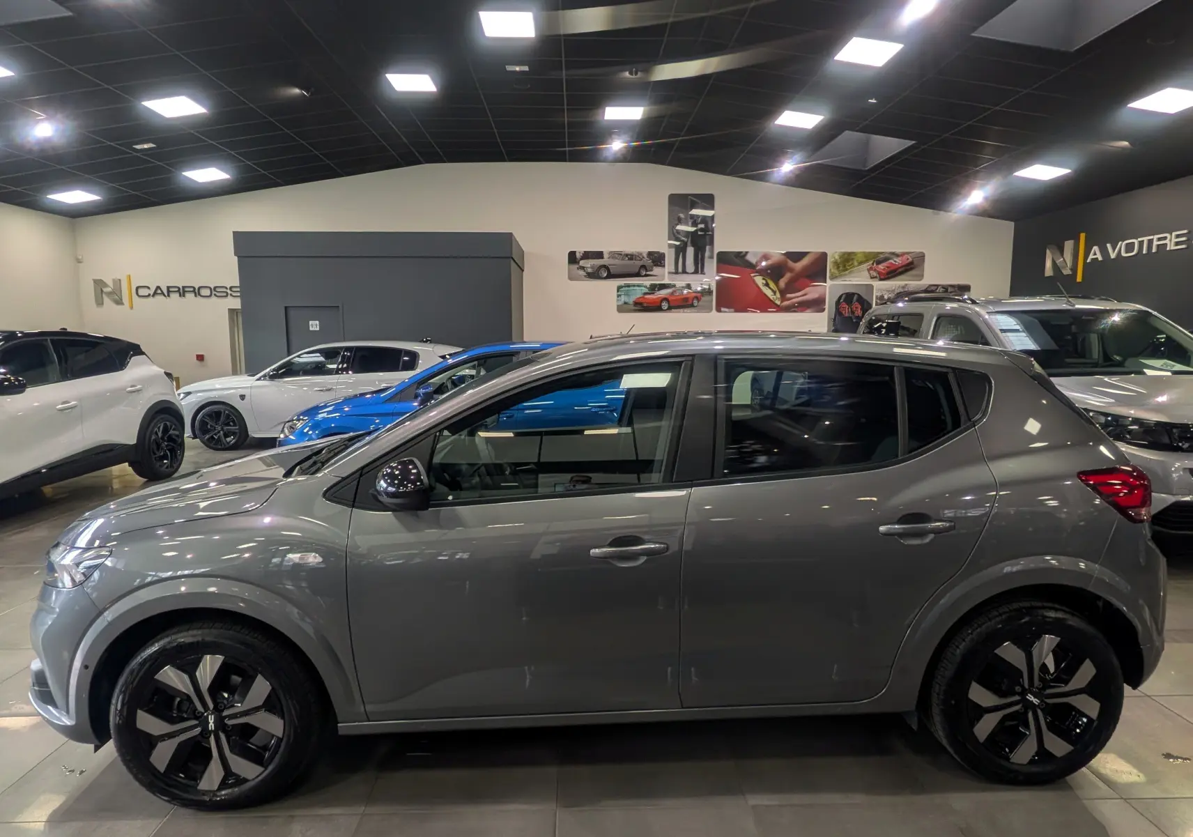 Profil côté gauche d'une Dacia Sandero TCe 90 CH Journey gris schiste, avec jantes noires et grises, en intérieur showroom.