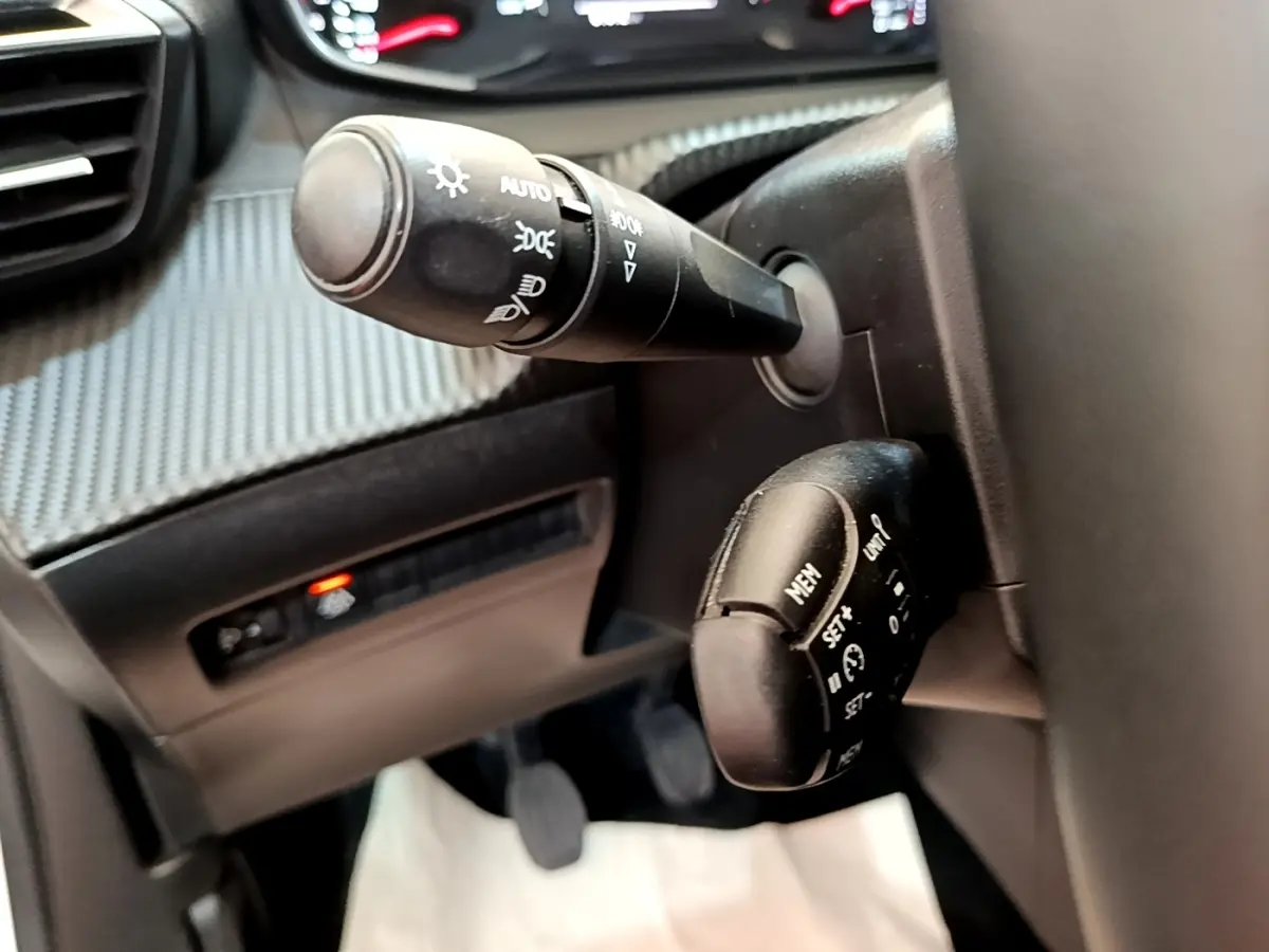 Gros plan sur les commandes de phares et régulateur de vitesse à gauche du volant dans l’habitacle d’un Peugeot 2008 blanc.