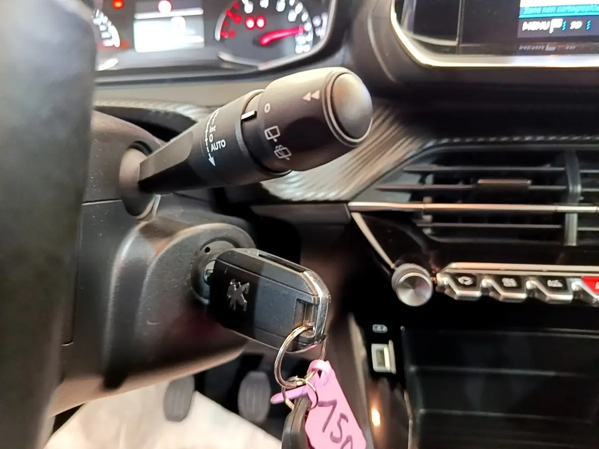 Gros plan sur le contacteur avec clé Peugeot insérée, volant cuir et tableau de bord noir du Peugeot 2008 blanc.