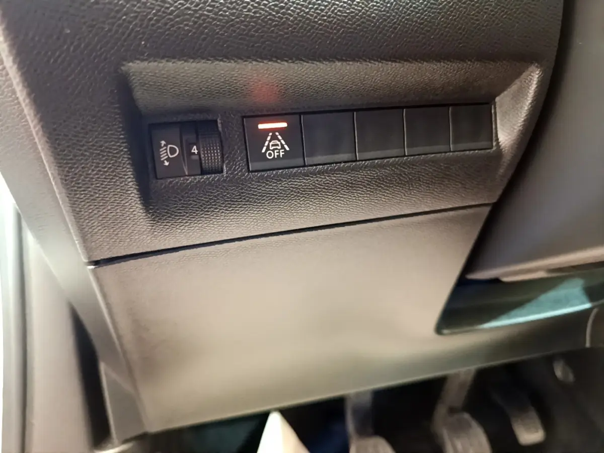Détail du tableau de bord côté conducteur du Peugeot 2008 blanc, avec commande de réglage des phares et désactivation de l'alerte de franchissement de ligne.