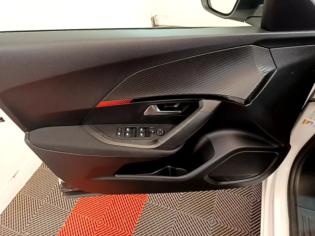 Vue intérieure du panneau de porte côté conducteur du Peugeot 2008 blanc, avec commandes électriques et insert décoratif noir.