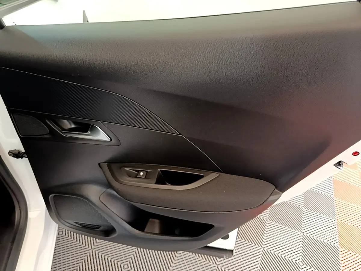 Vue intérieure du panneau de porte avant gauche de la Peugeot 2008 blanc, avec commande de vitre et poignée argentée.