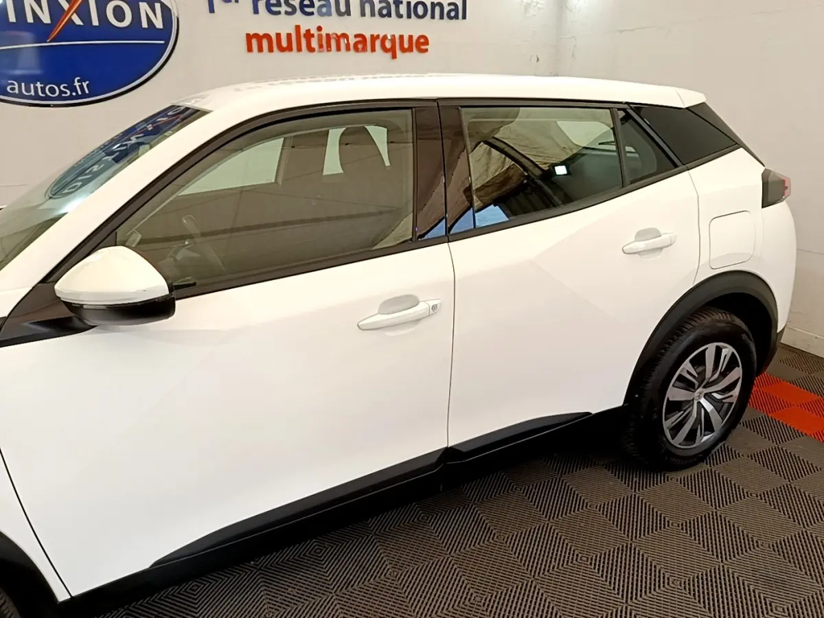 Vue de profil côté gauche d'un Peugeot 2008 blanc avec détails noirs sur les montants et jantes alliage.
