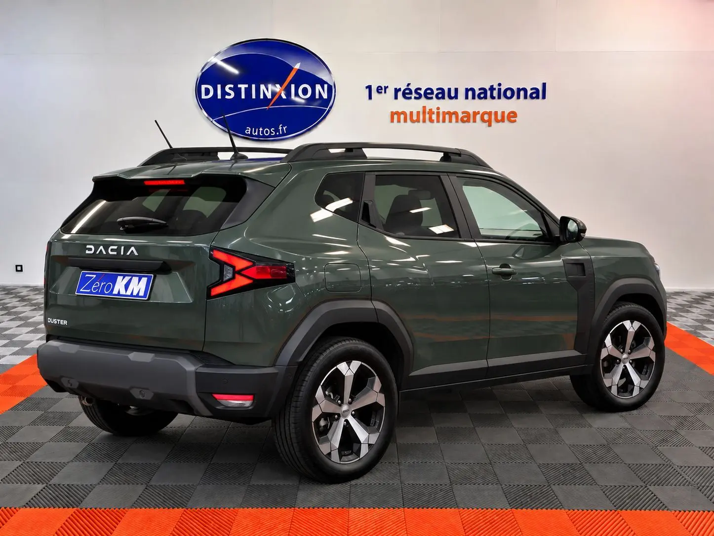 Vue 3/4 arrière droite du Dacia Duster 2026 vert cèdre avec jantes alliage et barres de toit noires.