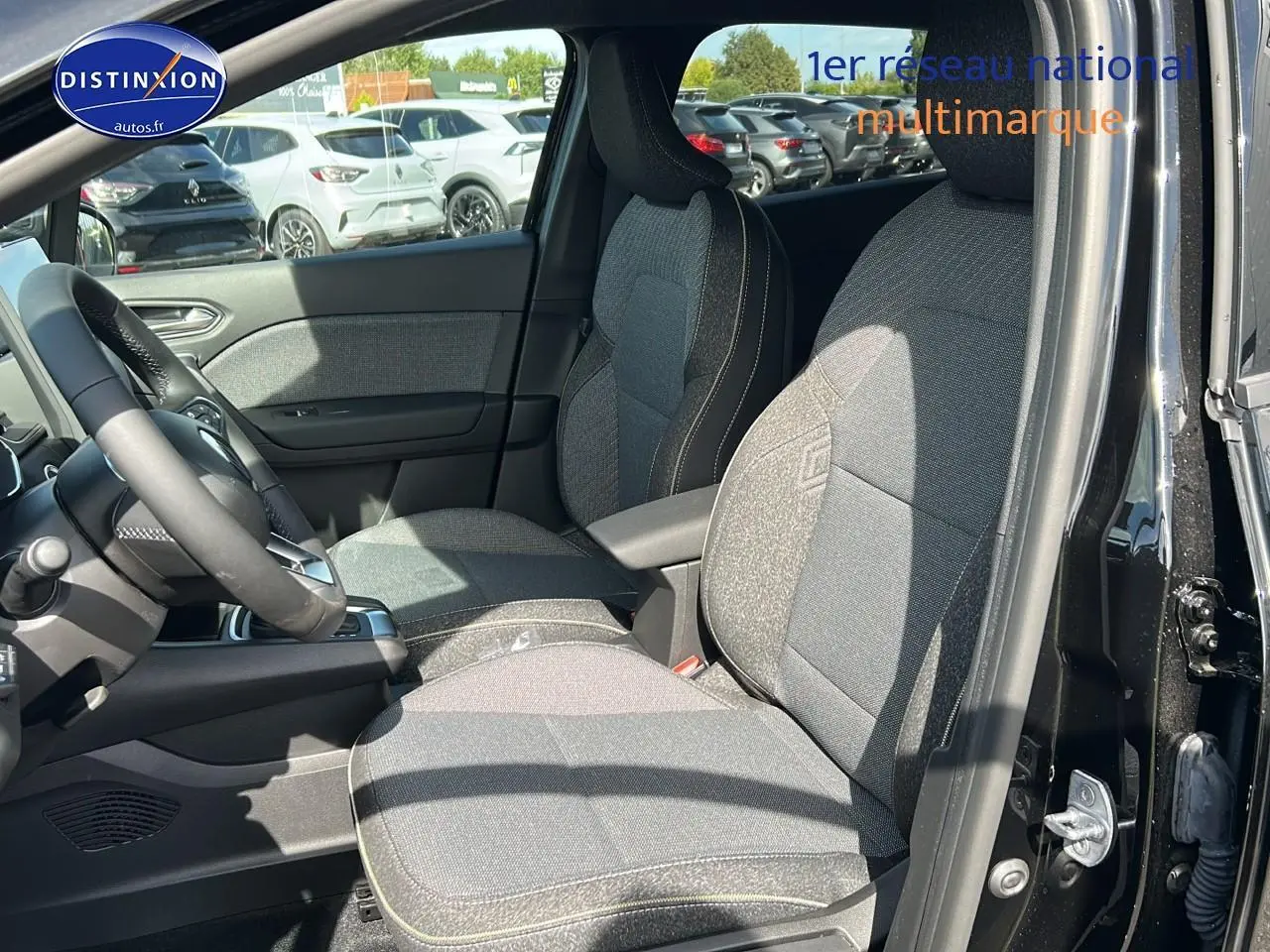 Vue intérieure côté conducteur du Renault Captur noir étoile 2025, mettant en valeur les sièges tissu gris et l'accoudoir central.