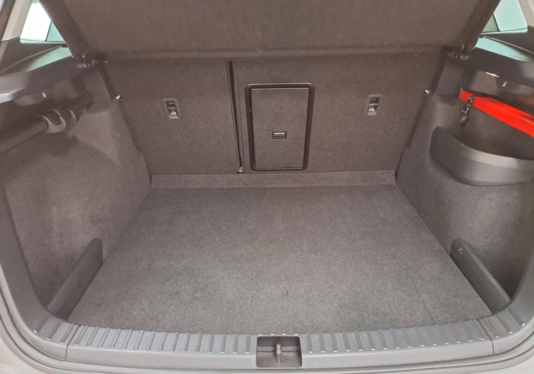 Coffre ouvert vu de face du Skoda Karoq gris perle, avec intérieur en tissu gris et rangement latéral rouge.