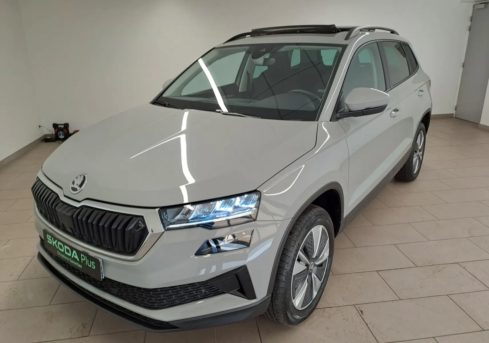 Vue 3/4 avant droite d'un Skoda Karoq gris perle 2023 avec toit ouvrant panoramique et jantes spécifiques.