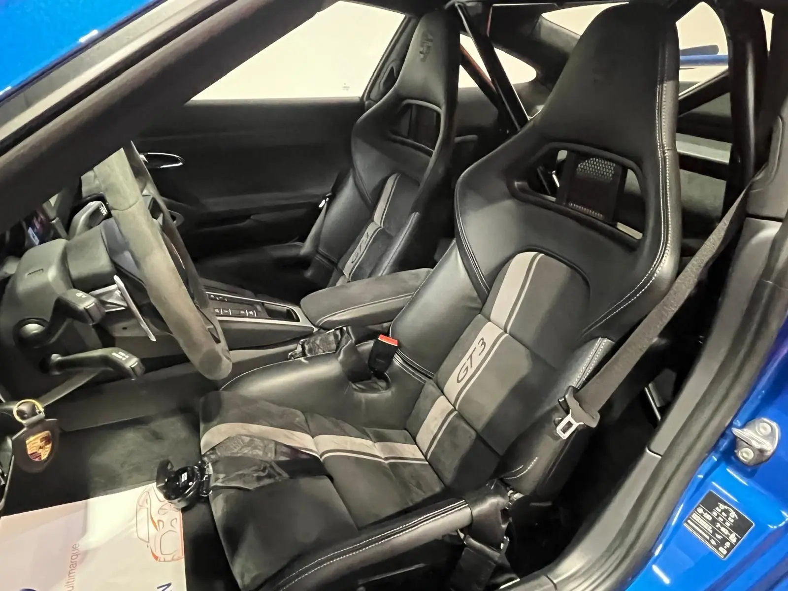 Vue intérieure côté conducteur de la Porsche 911 GT3 bleu saphir, avec sièges baquets sport et volant alcantara.