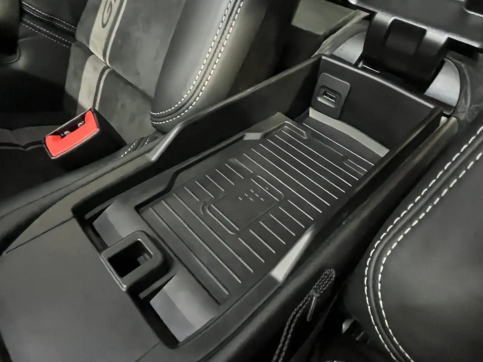 Gros plan sur la console centrale noire avec tapis antidérapant et surpiqûres blanches des sièges en cuir Alcantara.