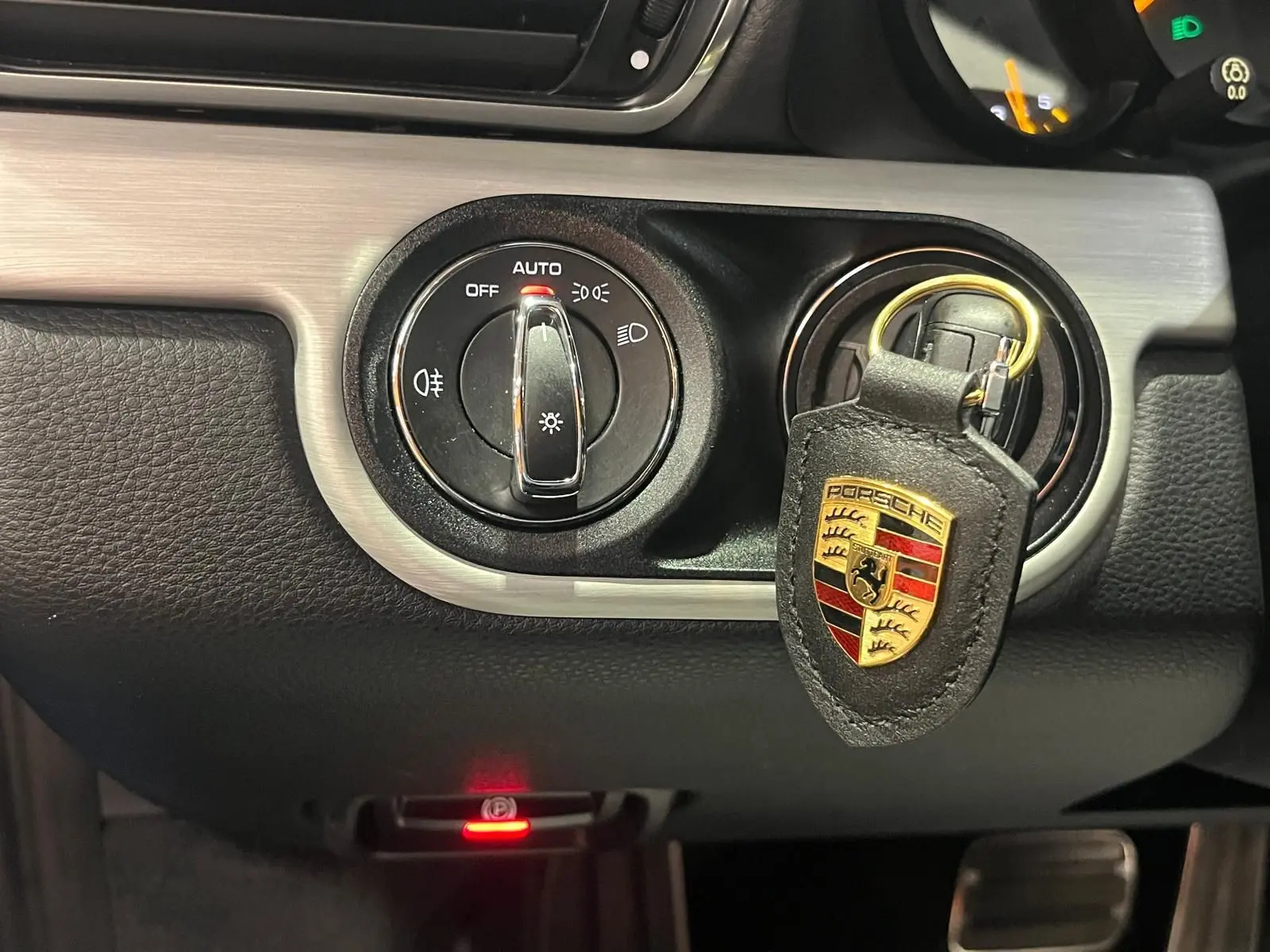 Détail intérieur montrant le contacteur d'éclairage et un porte-clés Porsche noir avec logo coloré.