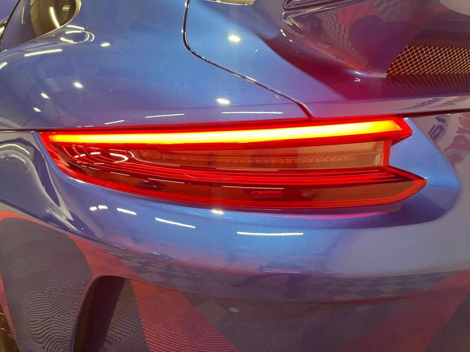 Gros plan sur le feu arrière droit d'une Porsche 911 GT3 bleu saphir, soulignant la finition sportive et les courbes élégantes.