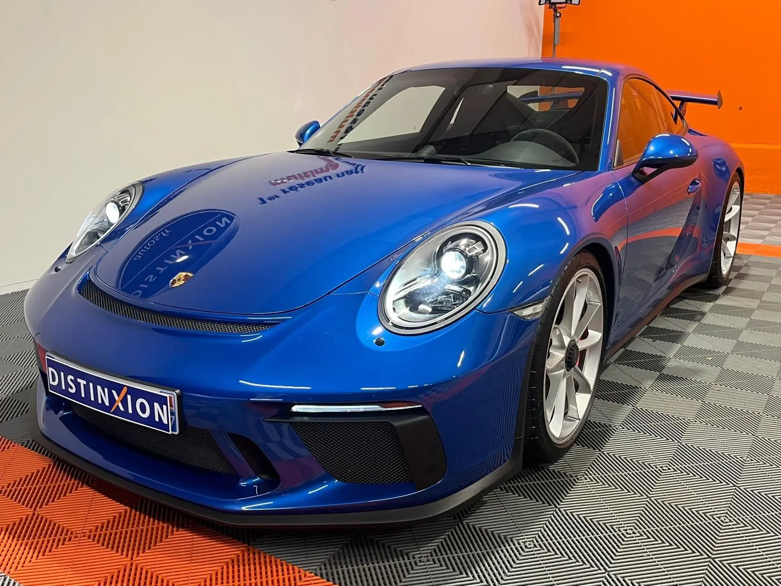 Porsche 911 GT3 bleu saphir vue 3/4 avant droit, avec jantes sport et aileron arrière visible.
