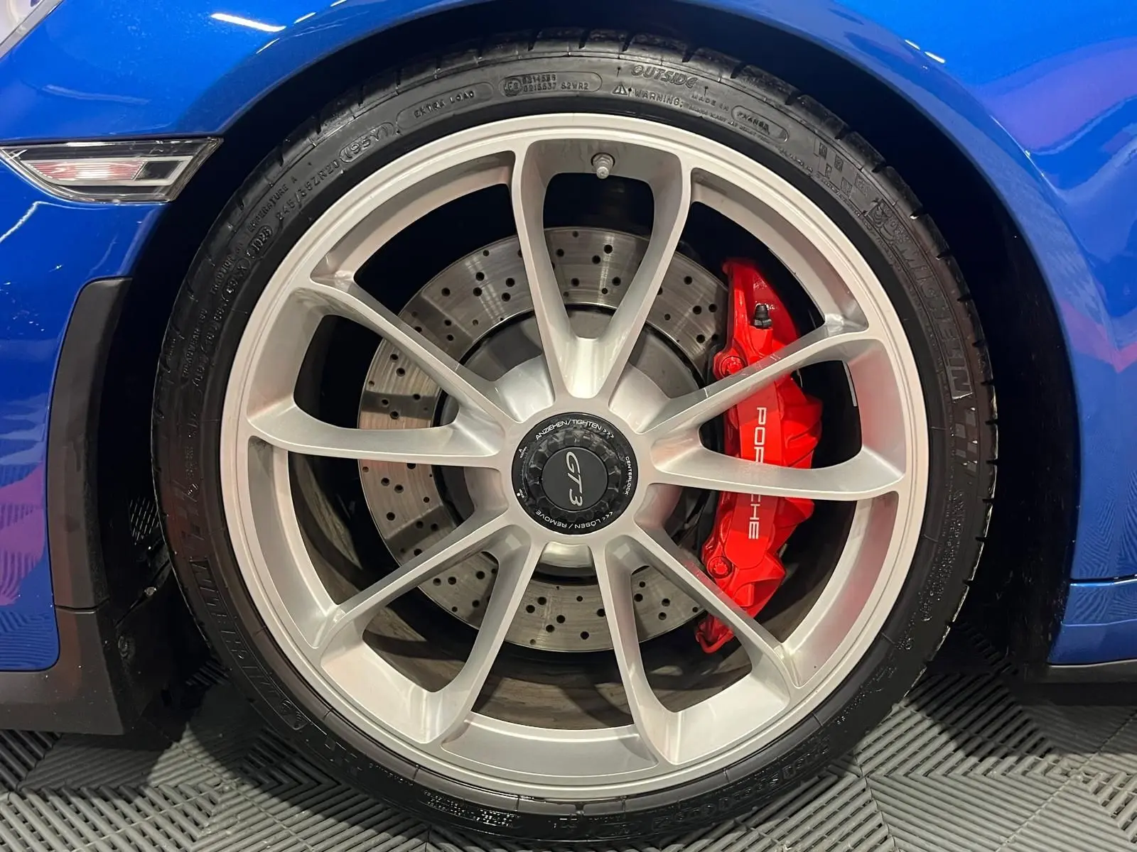 Gros plan sur la roue avant gauche d'une Porsche 911 GT3 bleu saphir avec étrier de frein rouge et jante argentée.
