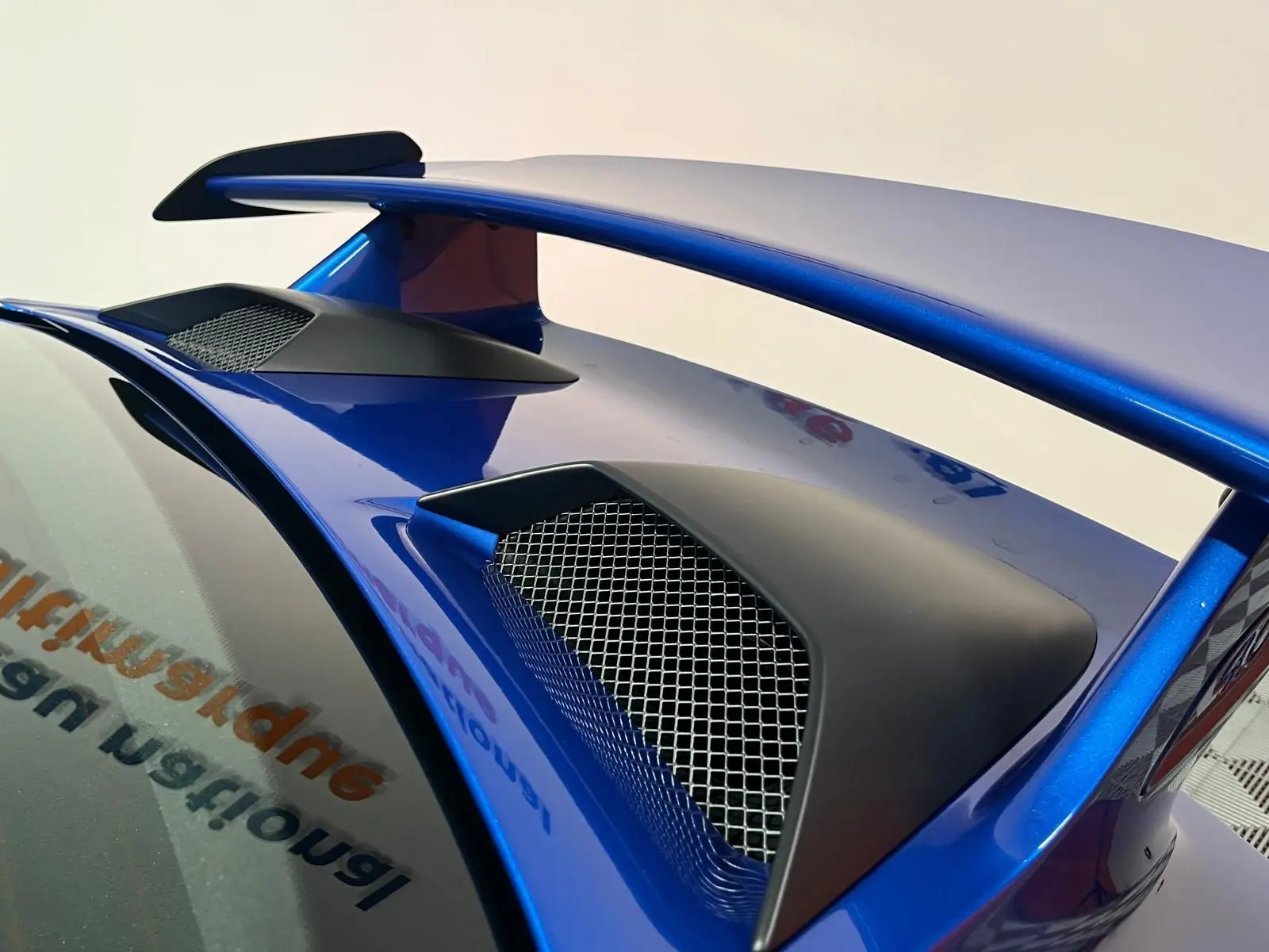 Gros plan sur l’aileron arrière bleu saphir de la Porsche 911 GT3 avec prises d’air noires et grille métallique.
