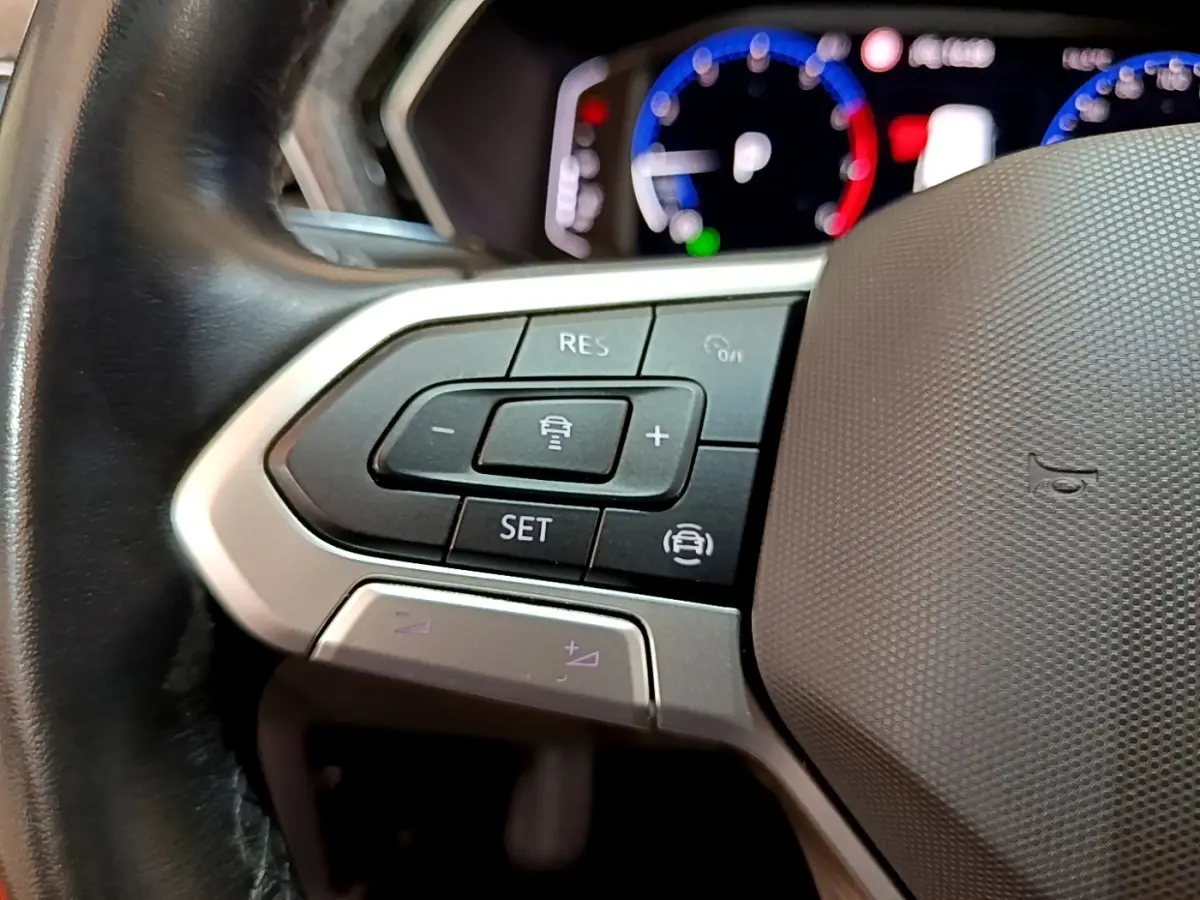 Gros plan sur les commandes du volant noir du Volkswagen T-Cross 2022, avec tableau de bord numérique flou en arrière-plan.