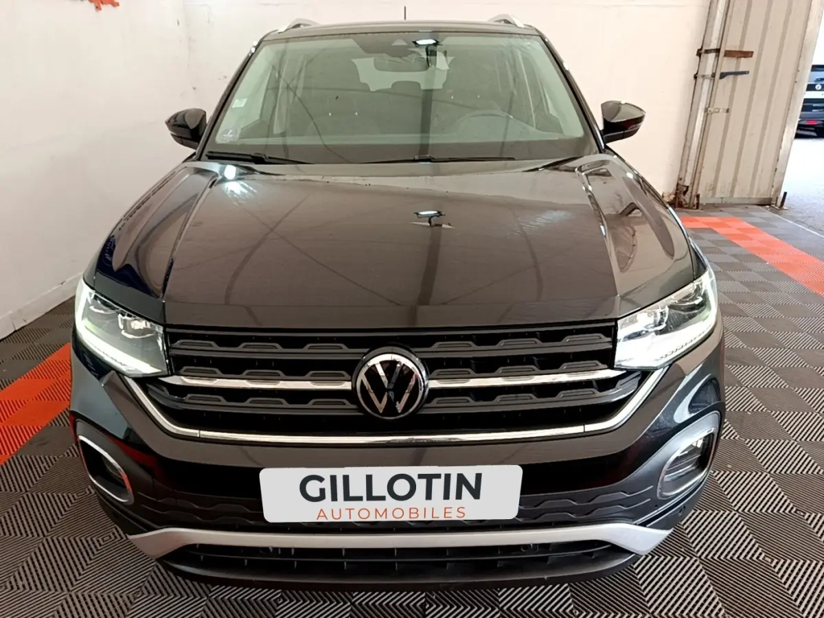 Vue avant d’un Volkswagen T-Cross noir 2022 avec calandre chromée et phares LED allumés dans un garage.