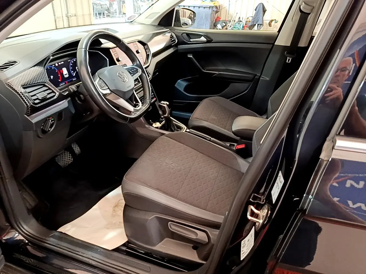 Intérieur avant côté conducteur du Volkswagen T-Cross noir, avec tableau de bord digital et sièges tissu gris.