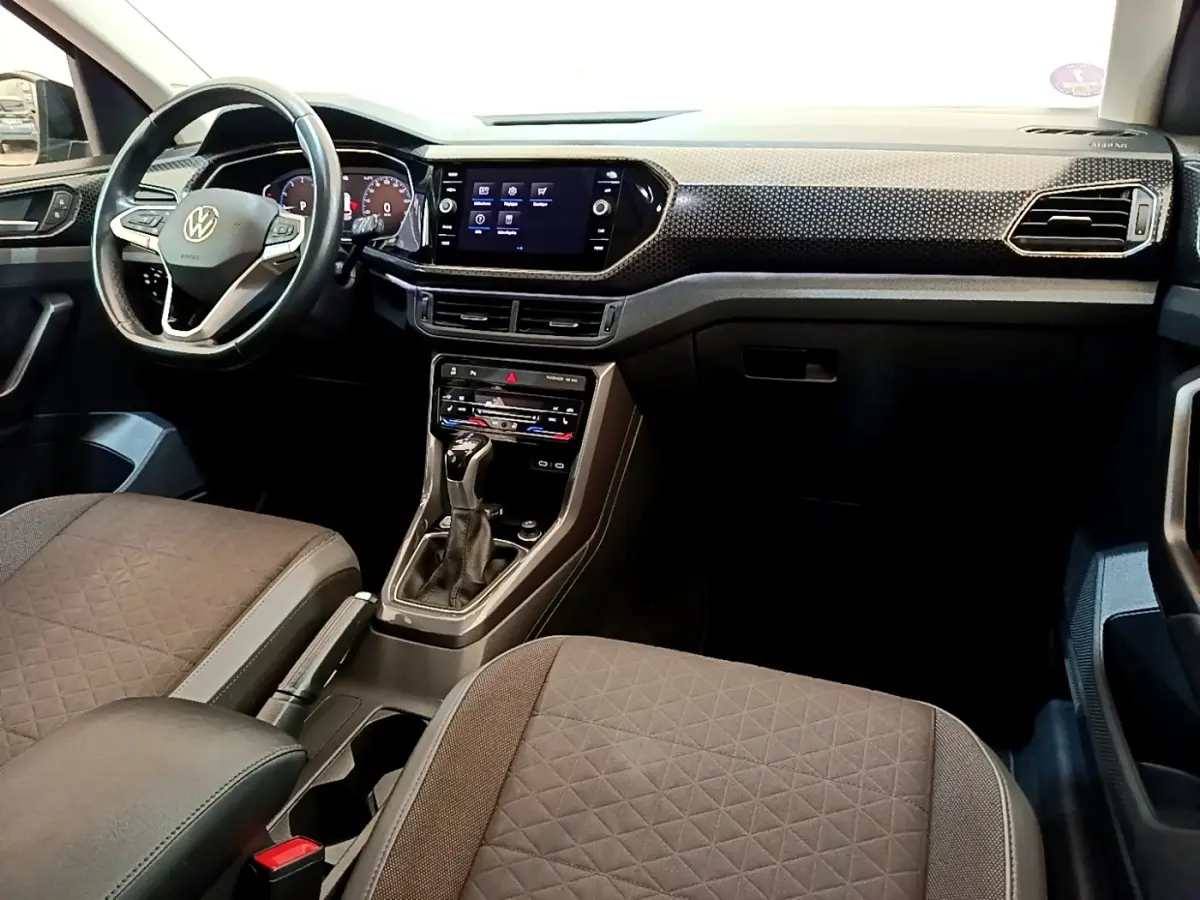 Vue intérieure avant du Volkswagen T-Cross 1.0 TSI 110ch DSG Carat 2022, tableau de bord noir avec écran tactile central.