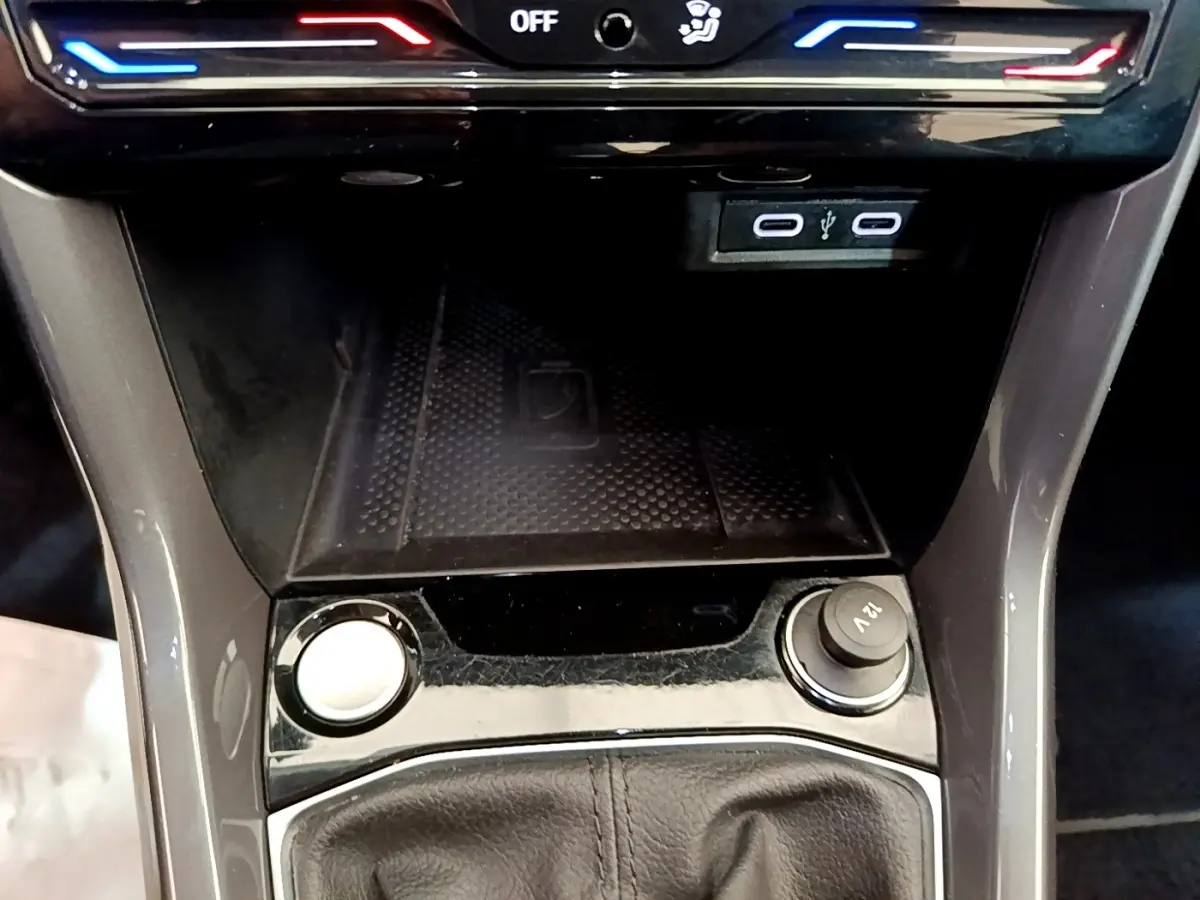 Vue rapprochée de la console centrale du Volkswagen T-Cross noir, avec zone de recharge sans fil et prises USB visibles.